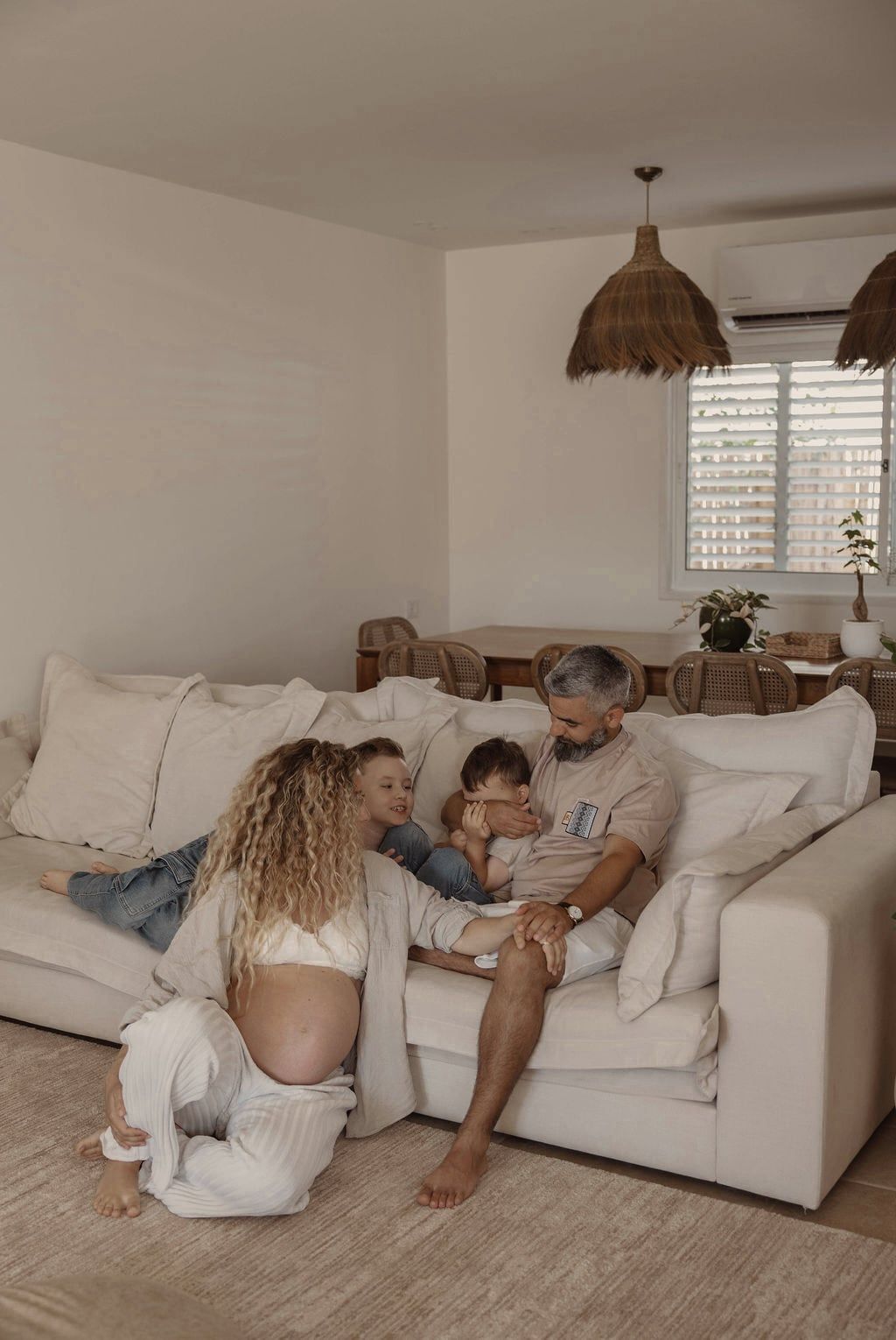 צילומי משפחה בבית באילת: אמא בהריון יושבת על השטיח ליד הספה, ושני הבנים ואבא לידה על הספה בסלון